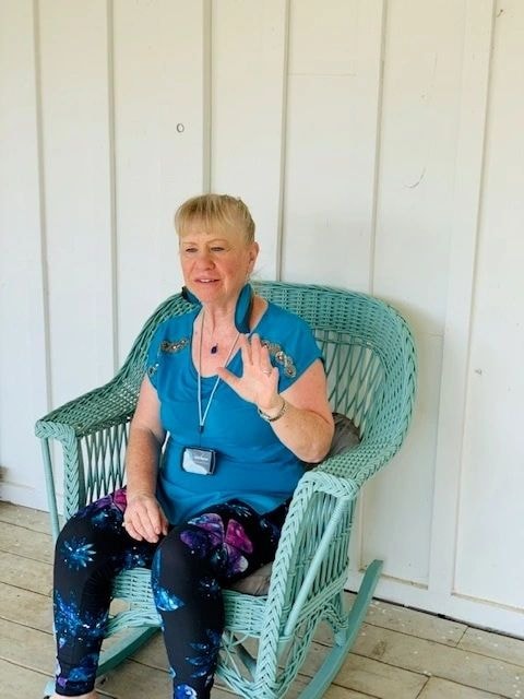 Vicki Reeve sitting in a wicker chair waving